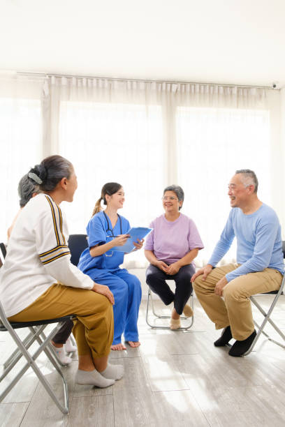 The caregiver therapist sits with a group of Asian senior people in a circle for checking physical and mental health in a group elderly therapy session. The nursing home facilitates a support group